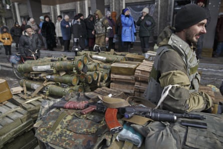 Residents line up waiting for a delivery of aid as a Russia-backed rebel guards a pile of weapons and ammunition outside an administration building