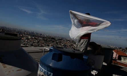A man places a mosquito net over a water container on his roof. Brazilians are hoarding water in their apartments, drilling homemade wells and taking other emergency measures to prepare for forced water rationing.