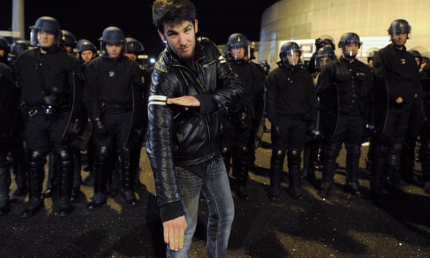 A man performs a "quenelle" salute next to a line of French police officers.