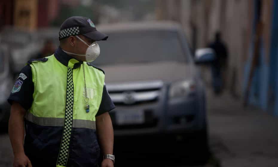 A traffic police officer covers his face with a mask as he works on a street covered covered with ash.