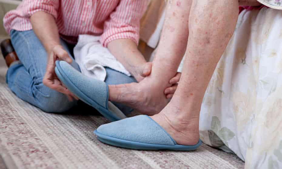 Close-up of woman helping elderly woman put on slippers