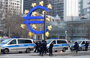 Police stand in front of the logo of the Euro at the European Central Bank