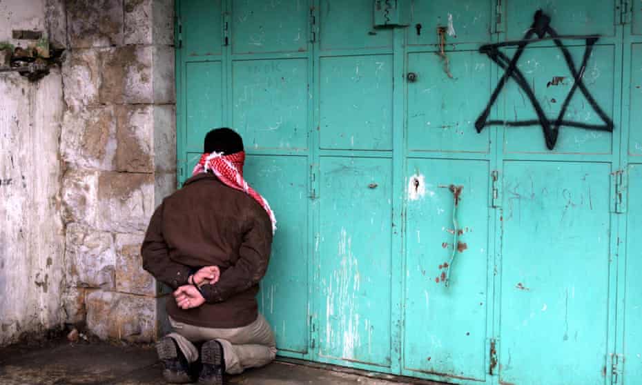 A blindfolded and handcuffed Palestinian kneels against a door with a spray-painted Star of David, after he was arrested by Israelis in January 2006, in the West Bank town of Hebron.