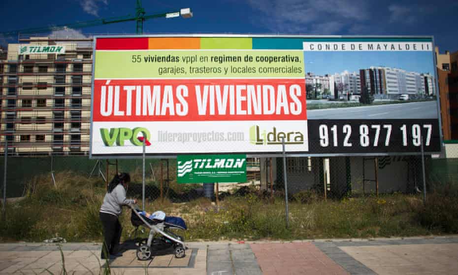 A pedestrian pushes a pram past a hoarding advertising new residential apartments in Madrid.