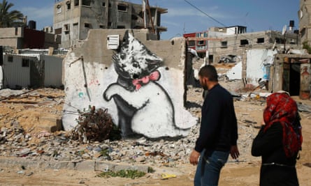 Palestinians walk past a mural of a playful kitten, thought to be painted by Banksy.