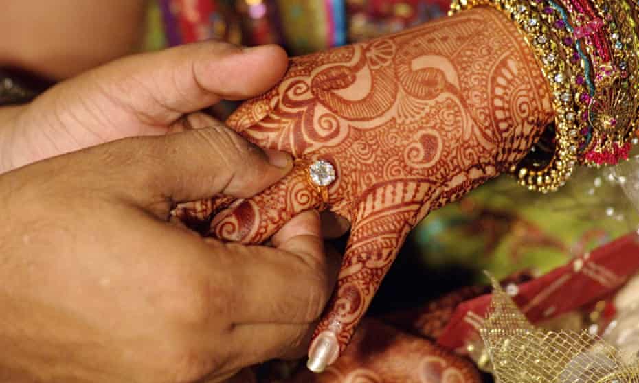 A bridegroom giving a wedding ring to a bride with hands decorated with henna and bangles, India