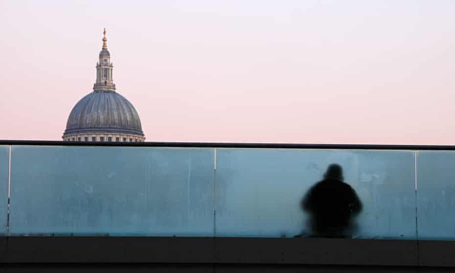 A homeless man sitting on Millenium bridge, with St. Paul's cathedral dome in the background.