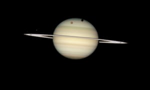 A rare moon transit of Saturn, which allowed Hubble to capture the shadow of the giant orange moon Titan on Saturn’s north polar hood. Below Titan and to the left is the moon Mimas, casting a much smaller shadow onto Saturn’s equatorial cloud tops. Farther to the left, and off Saturn’s disk, are the bright moon Dione and the fainter moon Enceladus. 