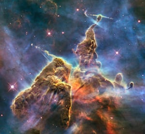 This area of the Carina Nebula is know as Mystic Mountain. In this composite image we see the chaotic activity atop a three-light-year-tall pillar of gas and dust that is being eaten away by the brilliant light from nearby bright stars. Jets of gas are also being fired from within the pillar by infant stars.