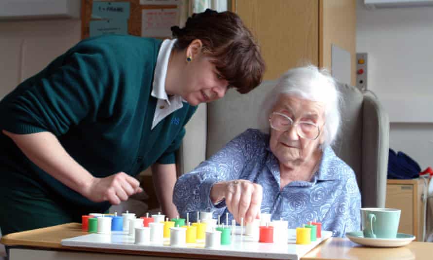 A nurse helps an elderly patient to play solitaire