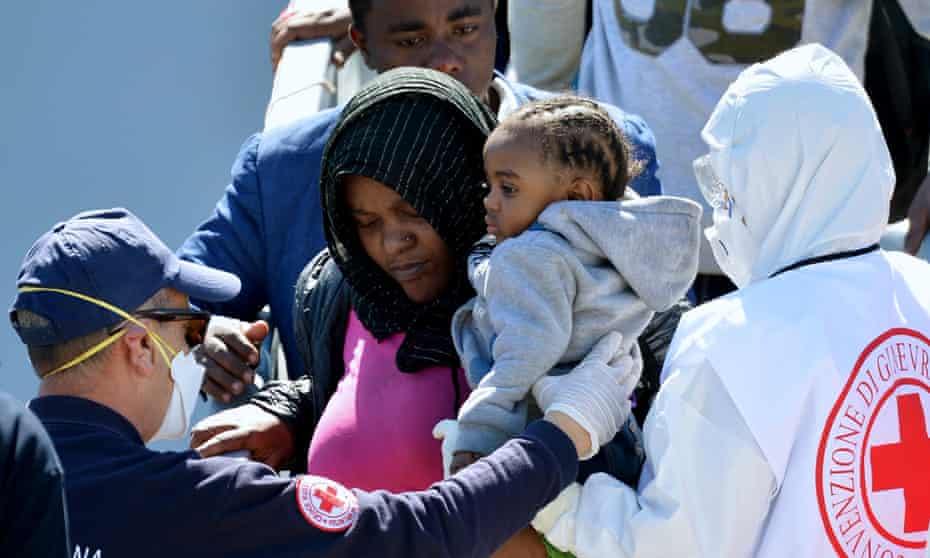 Rescued migrants are helped from an Italian navy ship after arriving in Augusta, Sicily.