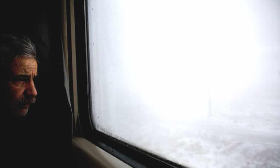 A man looks out through a train window at a snowy scene in northern Iran