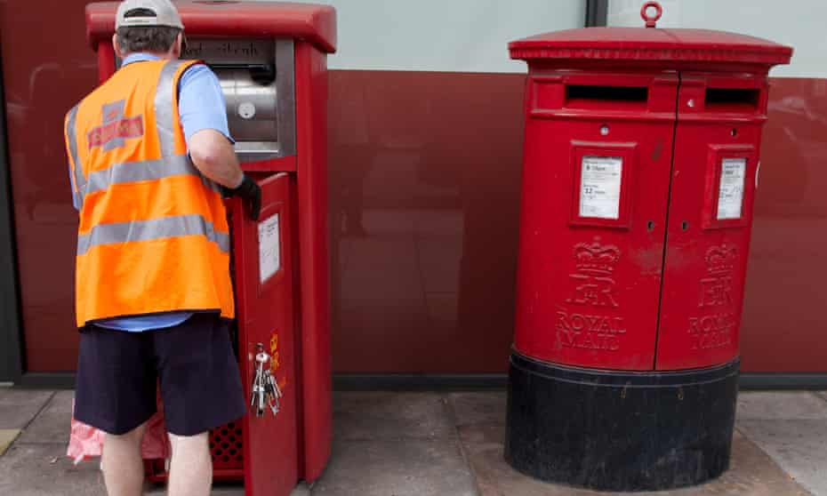 A postal worker empties a postbox in London