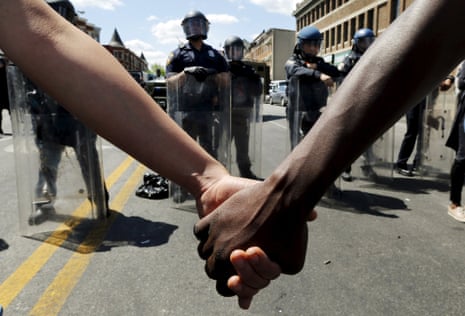 Members of the community hold hands in front of police officers in riot gear outside a recently looted and burned CVS store in Baltimore.
