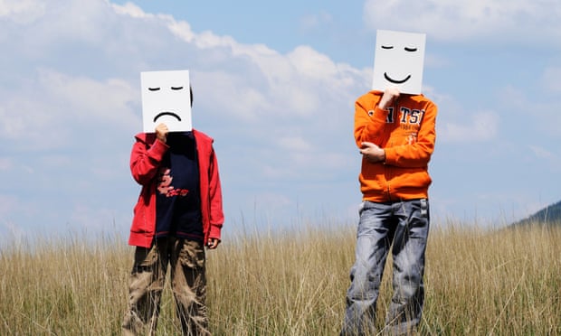 Boys in a field holding happy and sad facial expressions