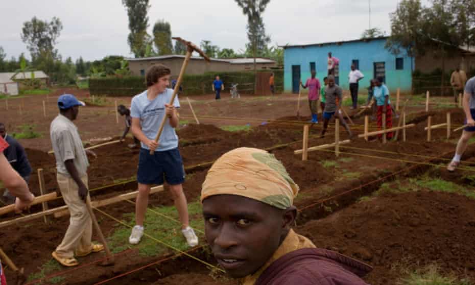 An English public schoolboy helps locals in a Rwandan village dig a foundation for a new multipurpose hall.