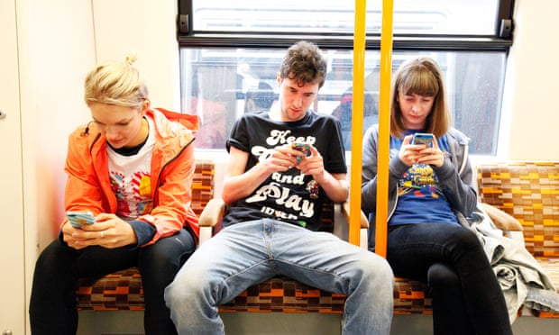 Three people absorbed in their phone on the tube.