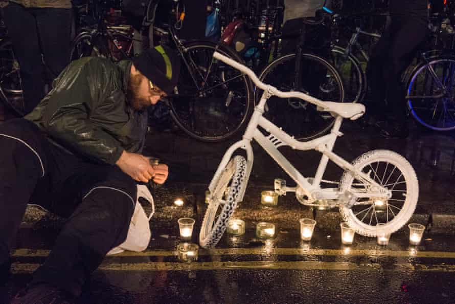 A man lights candles beside a "ghost bike" memorial in London.