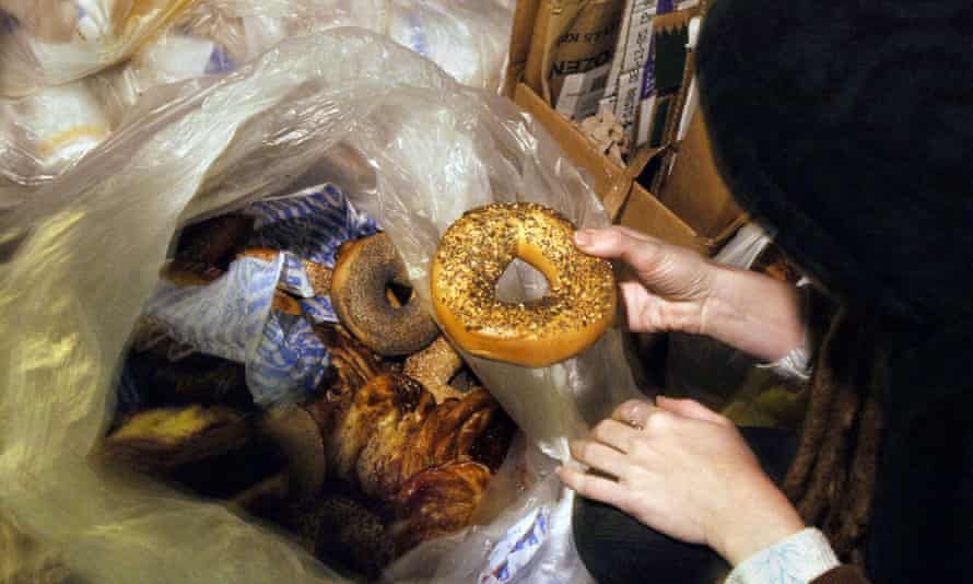 A woman holds a bagel she found in a garbage bag of pastries and bagels outside a shop in Manhattan.