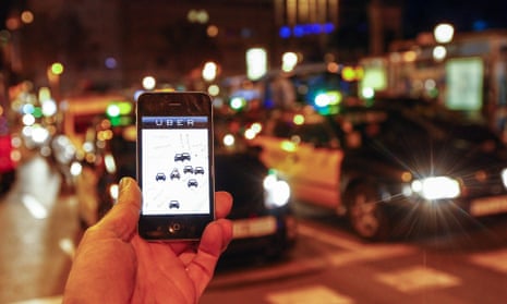 A man holds an iPhone displaying the Uber app in front of a queue of traffic. 