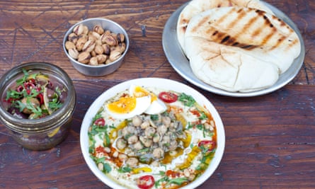 Olives, pistachios and hummus with chickpeas, chilli and pine nuts on a wooden platter.