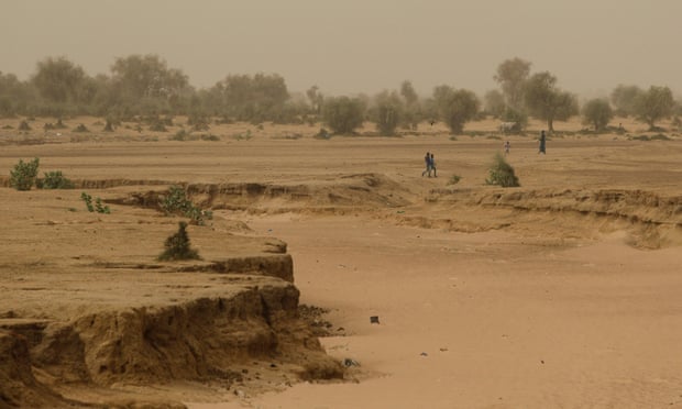 People walk past a dry riverbed in the Matam region of northeastern Senegal in the Sahel region of North Africa. 