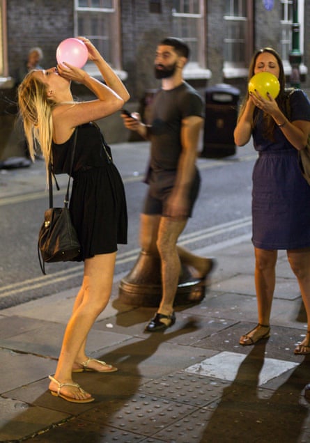 Revellers take laughing gas in an east London street where it is openly sold for around £3 a go.