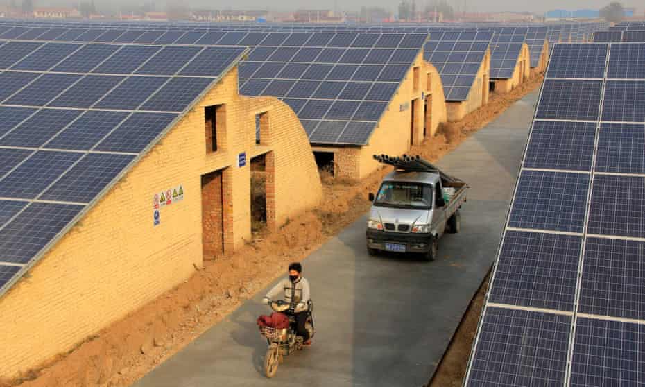 A resident on an electronic bicycle and a truck travel past solar panels on the roof of greenhouses growing mushrooms in Neihuang county, Henan province