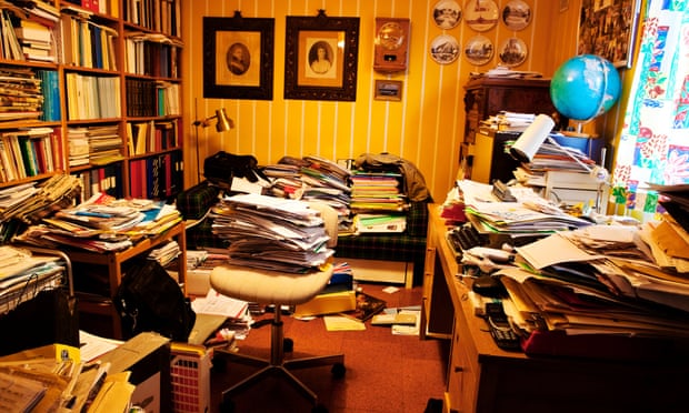A private study with piles of papers covering every surface and on the floor.