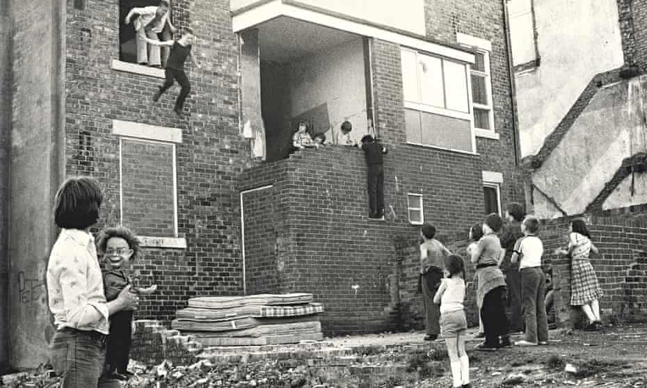 Boys jump from a second storey window of a derelict house while other children watch