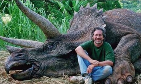 Picture of Steven Spielberg sitting next to a 'dead' dinosaur prop.