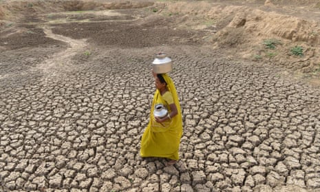 An Indian woman carries an empty water pot as she crosses the dry bed of a pond at Mehmadpur village.