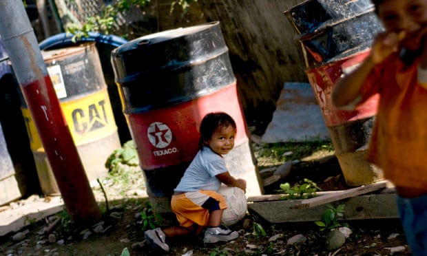 A child from the Huaorani tribe, also known as the Waos, who are native Amerindians from the Amazonian Region of Ecuador, plays near a discarded Texaco oil drum