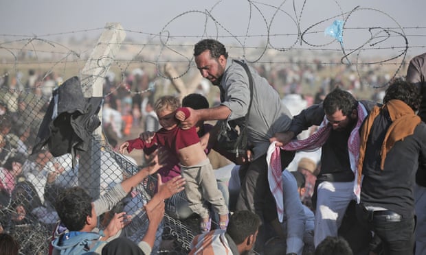 A  June 14, 2015 file photo of a Syrian refugee carrying a baby over the broken border fence into Turkey after breaking the border fence and crossing from Syria in Akcakale, Sanliurfa province, southeastern Turkey. The mass displacement of Syrians across the border into Turkey comes as Kurdish fighters and Islamic extremists clashed in nearby city of Tal Abyad.