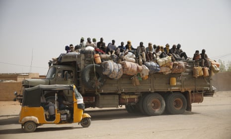 Migrants sit on their belongings in the back of a truck as it is driven through a dusty road in the desert town of Agadez, Niger