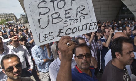 A striking taxi driver holds a placard which read, "Stop Uber, Stop listening," referring to the new US spying report in France, during a taxi drivers demonstration in Paris, France, Thursday, June 25, 2015. French taxis are on strike around the country, snarling traffic in major cities and slowing access to Paris' Charles de Gaulle airport after weeks of rising and sometimes violent tensions over Uber. (AP Photo/Michel Euler)