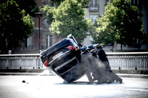 French riot police attempt to flip an overturned car back onto its wheels during the protest against Uber in Paris.
