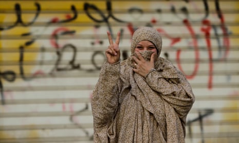 A Bahraini pro-democracy protester gestures in front of a wall sprayed with anti-government graffiti.