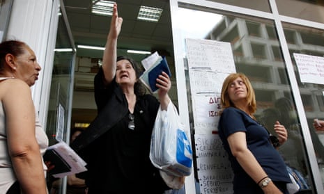 A woman gestures at the entrance of EOPYY office, while other people wait to receive their prescribed medicines in Athens.