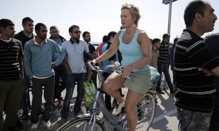 A tourist rides her bicycle past migrants waiting outside the police station.