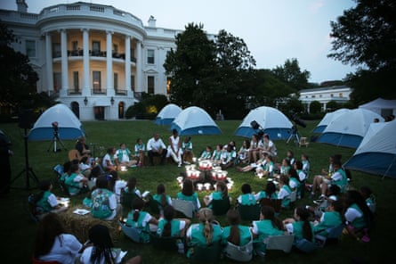 Girl Scouts and the Obamas form a singing circle with the White House in the background.