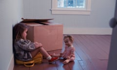 A girl sits next to a cardboard box with her doll