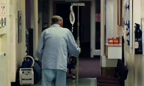 An elderly patient attached to a drip walks along a hospital corridor