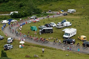 The pack of riders pass a collection of spectators different modes of transport