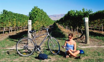 Woman sitting on ground next to her bicycle and checking map with vines behind.