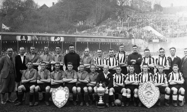 Norwich City, in plain shirts, pose at the Nest in 1934 with their trophies from winning the Second Division and the local Hospital Cup. They are joined by their opponents, Grimsby.