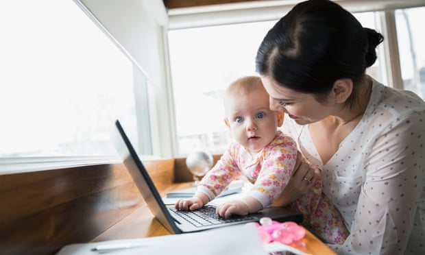 A woman holds a baby in her lap who plays with a computer