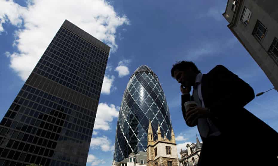 A man passes the Swiss RE building, also known as the Gherkin, in London.