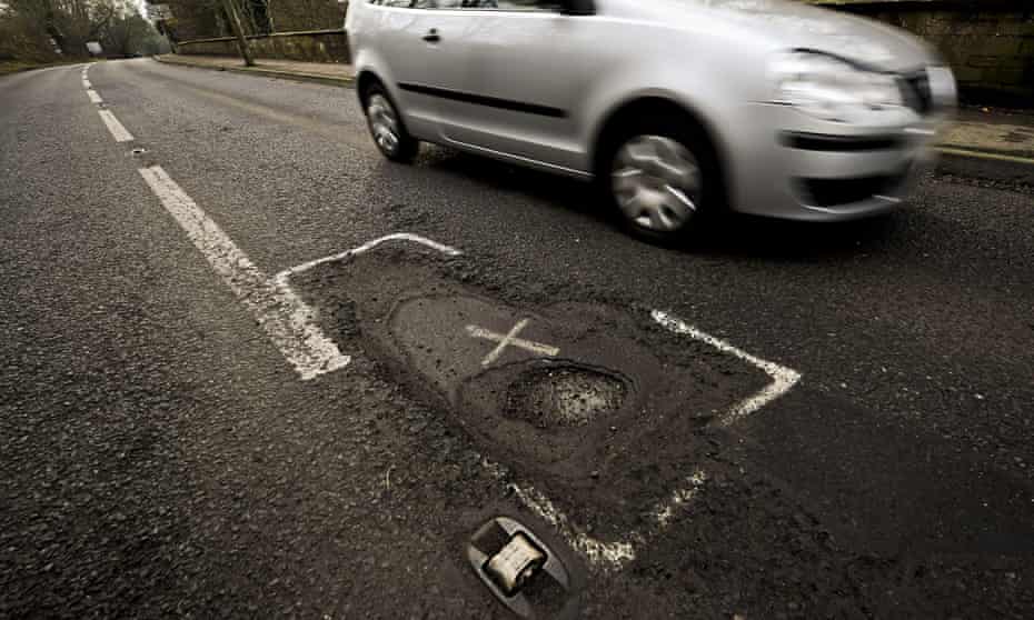 Car driving past a large pothole