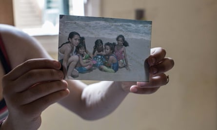 The hands and arms of a girl, with bitten nails and cuts, shown holding a photograph of a group of 6 girls on a beach smiling